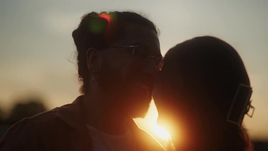 The silhouette of a man and woman close together with the setting sun glowing