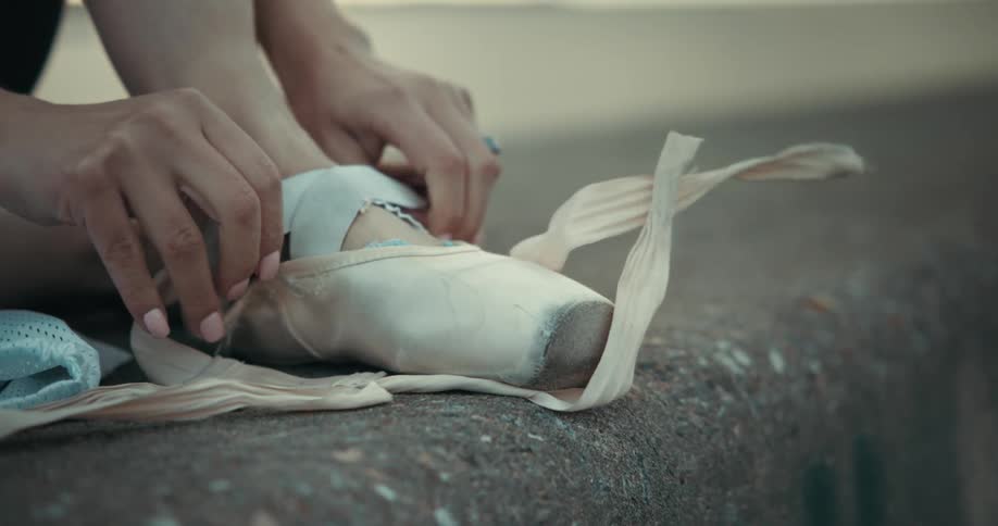 Close up of a woman sitting on the ground wearing a ballet shoe