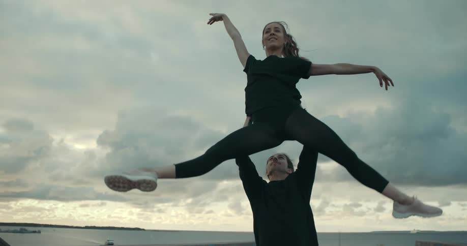 Man lifts up a ballet dancer on a wooden pier next to the ocean at sunset