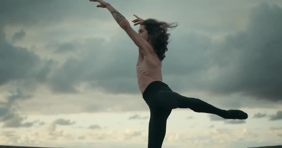 A man with tattoos on his chest and arms is dancing under a cloudy sky as a bird flies overhead