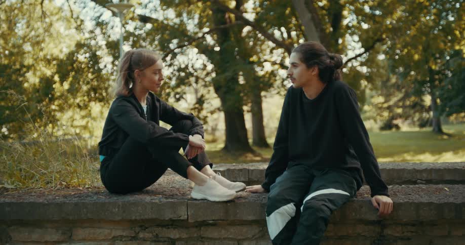 Two friends sitting on a park stone wall talking during a workout break