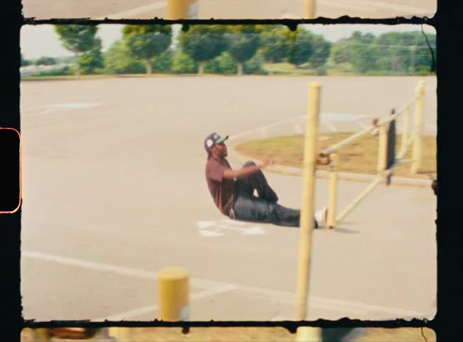 Vintage footage of man sitting on his skateboard and skating under a railing and falling off