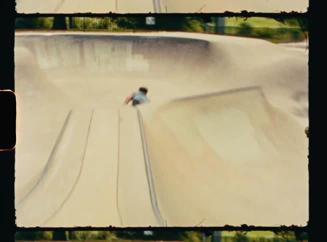 A young man wearing inline skates goes down the ramp of a skate park bowl