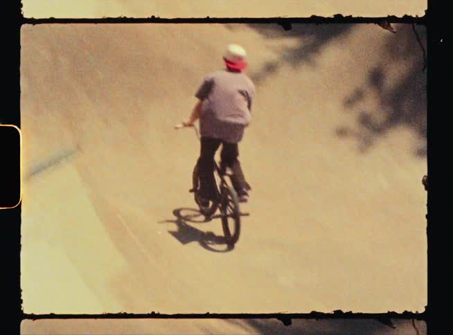 A young male in a baseball hat does jumps on his bike at a skate park