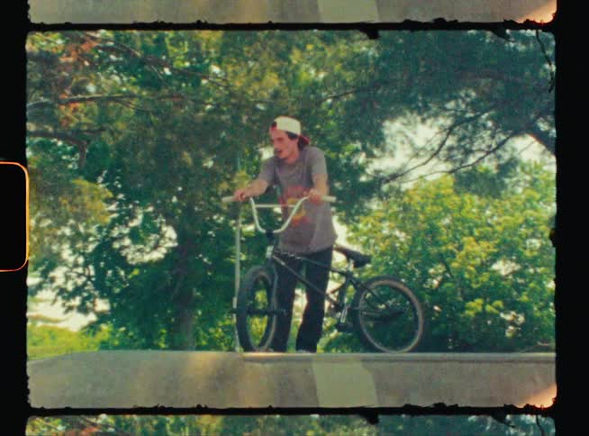 Vintage footage of a teenage boy standing at the top of a ramp with his bike
