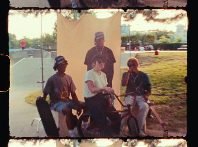 Youths sit together with skateboards and a bicycle near skate park