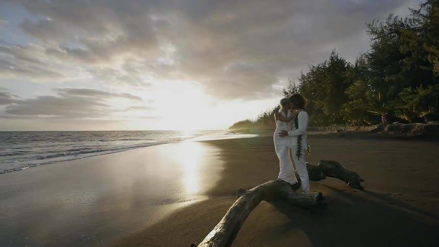 A couple dressed in white kissing on a beach during sunset