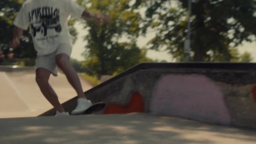 A young man rides a skateboard up a ramp and onto the edge of a wall at the skate park