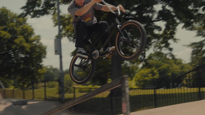 A young male in a baseball hat does a jump onto a rail with his bike at a skate park