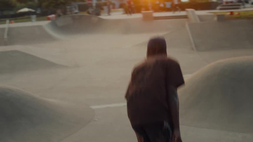 A teenage boy rides his skateboard down a slope in a skateboard park among other teenagers on skateboards