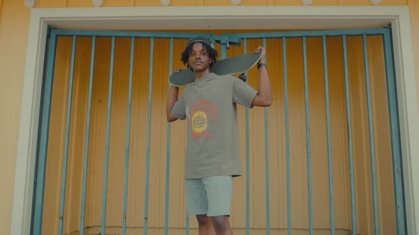 A man poses while holding a skateboard behind his head