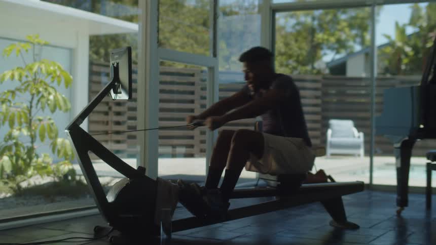 A man exercises using a rowing machine indoors during the day