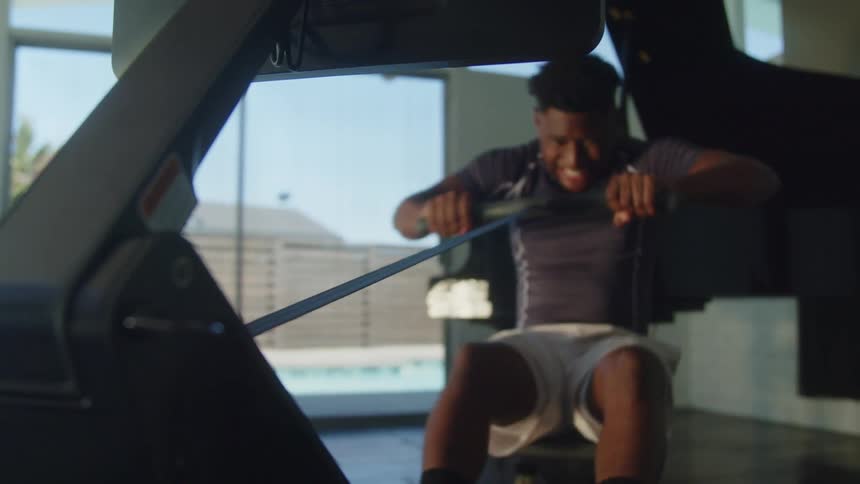 Man exercises in room with view of pool using a rowing machine