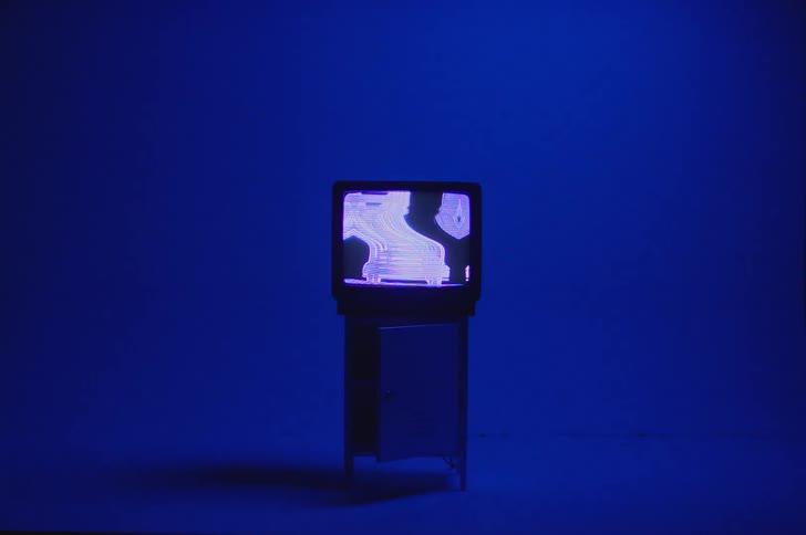 A television displaying a distorted image sitting on top of a small cabinet in a blue room