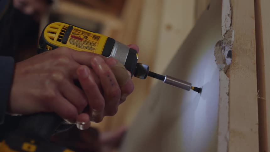 Construction worker uses screwdriver to attach dry board to building wooden frame