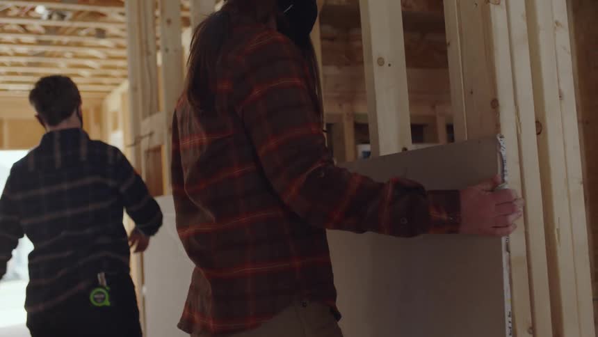 Construction workers place drywall against building framework