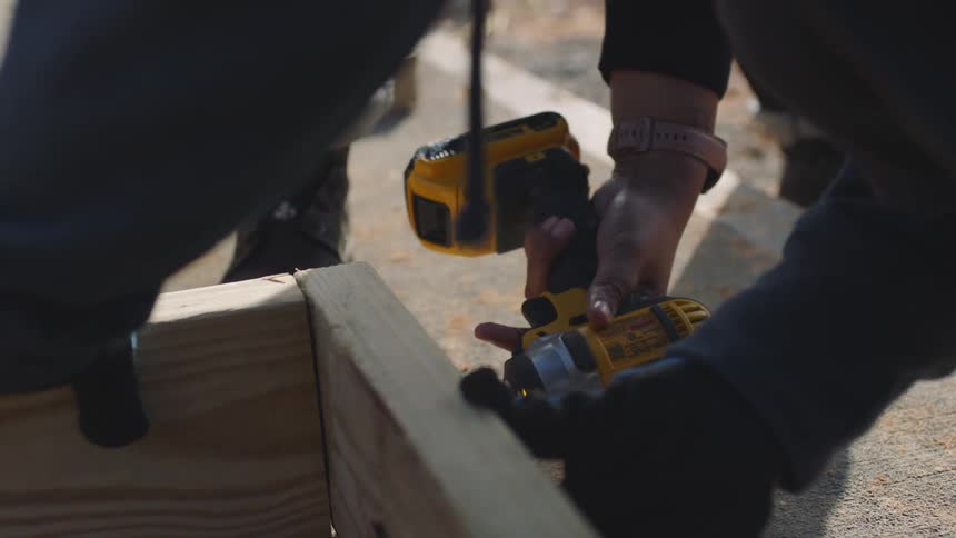 A construction worker uses an electric drill while working on assembling a wooden frame