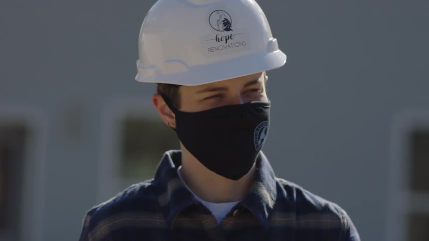 A construction worker stands outside with a mask and hard hat on