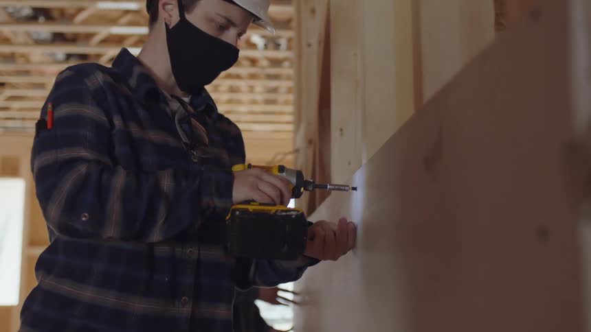 A construction worker uses a drill to attach wood to a wall