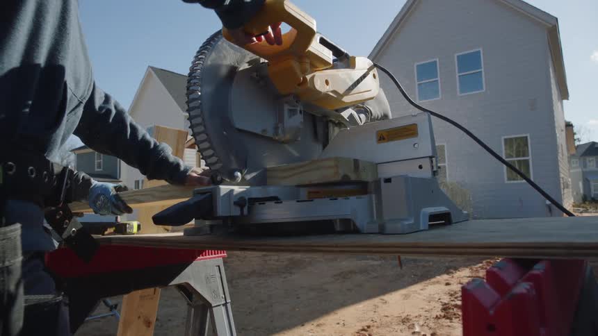 A construction worker cuts wood outside a house