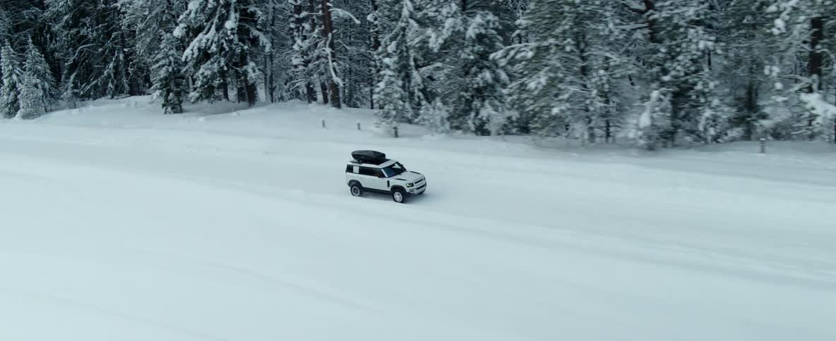 A vehicle drives on down a snow covered road next to a forest
