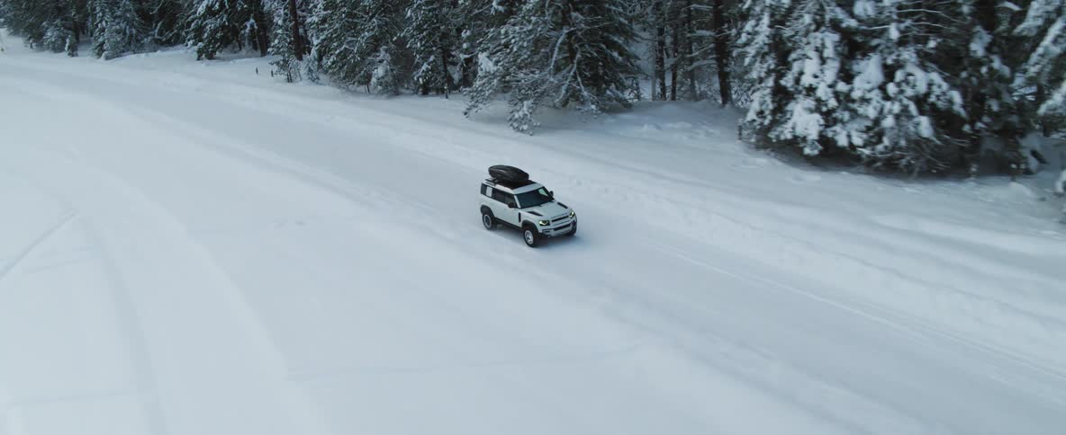 An automobile is traveling on a snow covered road near a forest on a winter day