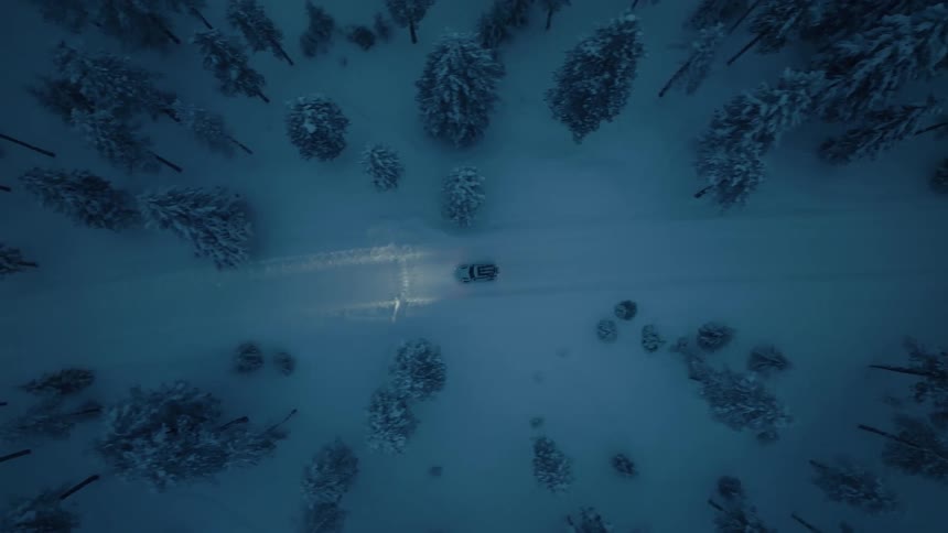 An suv traveling on a snow covered road through trees at dusk