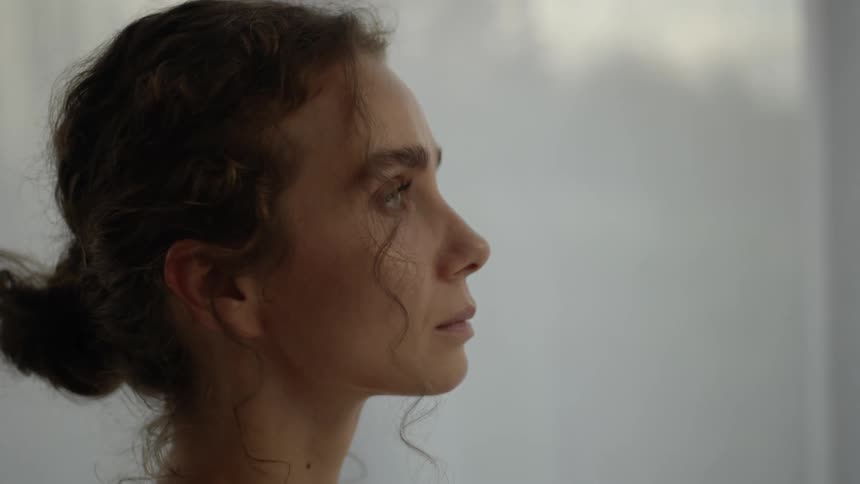 A woman slowly directs her gaze upwards and then looks off into the distance