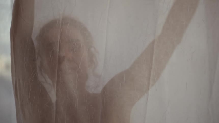 A woman stretching behind a sheer curtain at sunset