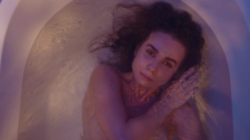 Top down view of a woman floating inside a bathtub under shimmering lights