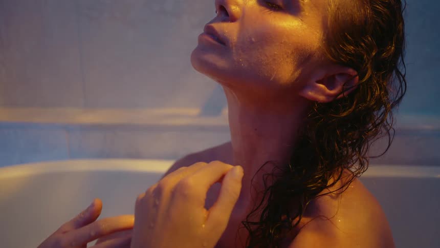 A woman sits in a bathtub and slowly caresses her hair with her hands