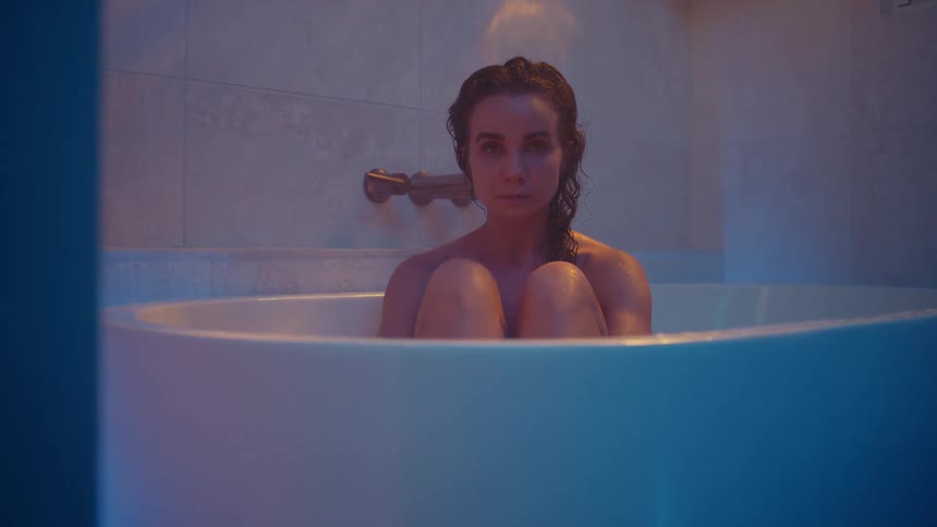 Filtered light plays over woman sitting in tub as she raises her head