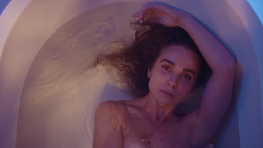 Woman sways back and forth while floating in bath as filtered light plays across her face