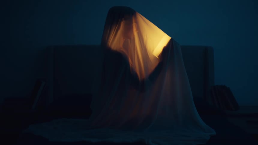 A woman sitting under a sheet on a bed holding a glowing light