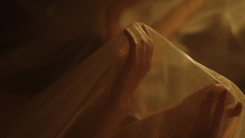 A dancers hands stretching sheer fabric while water reflects and distorts the light and shadow
