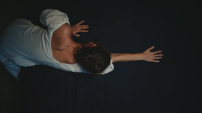 A woman in a white dress stretches her arms outward as she faces down