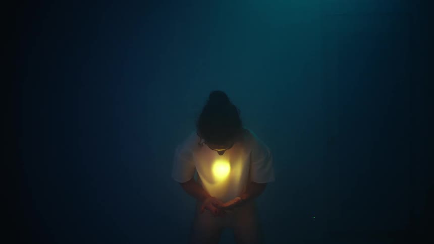 Surreal footage of young woman moving her hands over and around a flare under her shirt