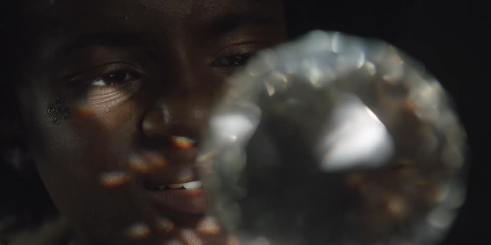 A woman smiles as a rotating white diamond like light shines geometric shapes on her face