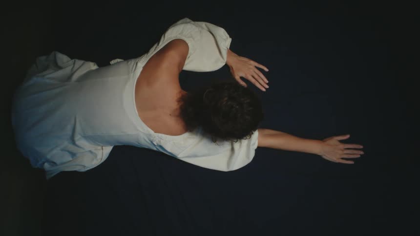 There is a young woman laying down and making hand movements