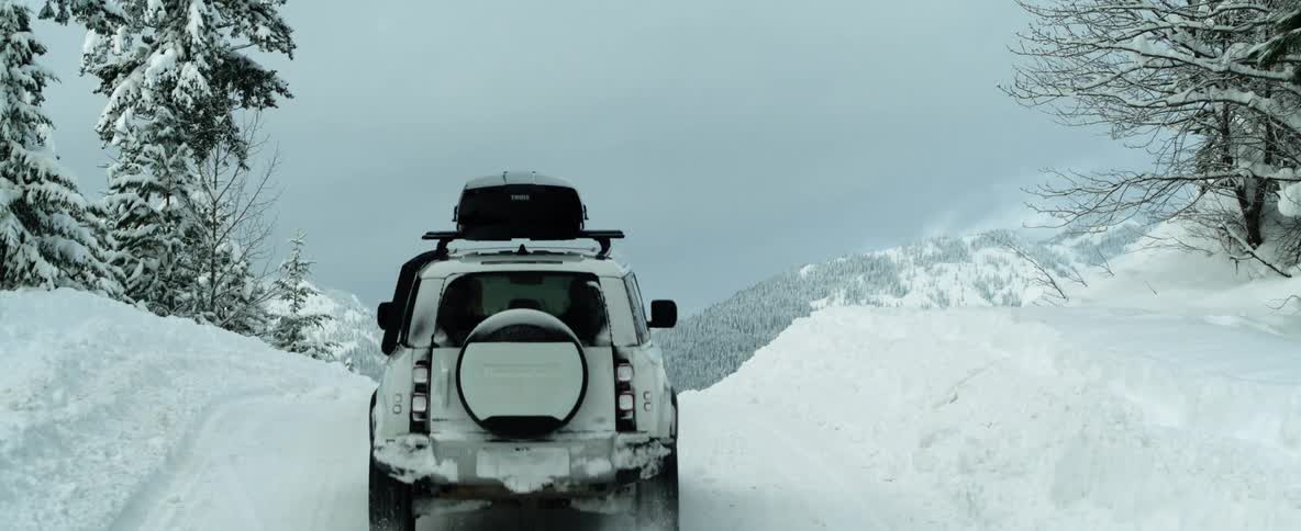 A vehicle travels up a snowy slope in the countryside on a cloudy day