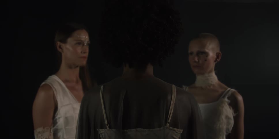 Models in neutral flowy dresses stand in a circle
