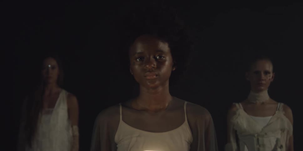 Woman in front holds light as two others stand behind her in dark area