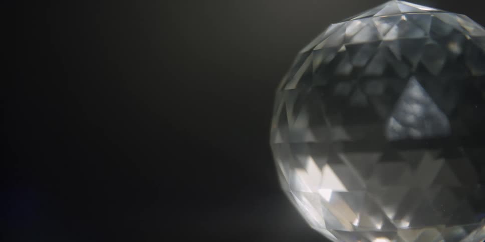 Light reflects from a rotating multifaceted cut glass globe in a dark room