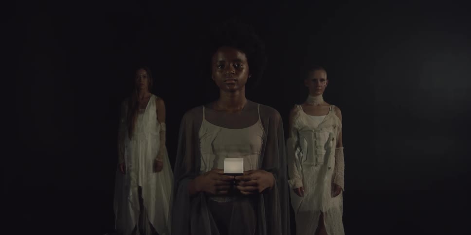 Two women are standing in the darkness behind a woman holding a glowing cube