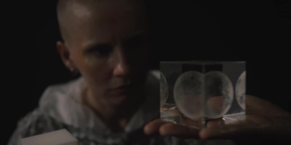 Someone is holding a clear cube with a sphere inside as a woman looks at it