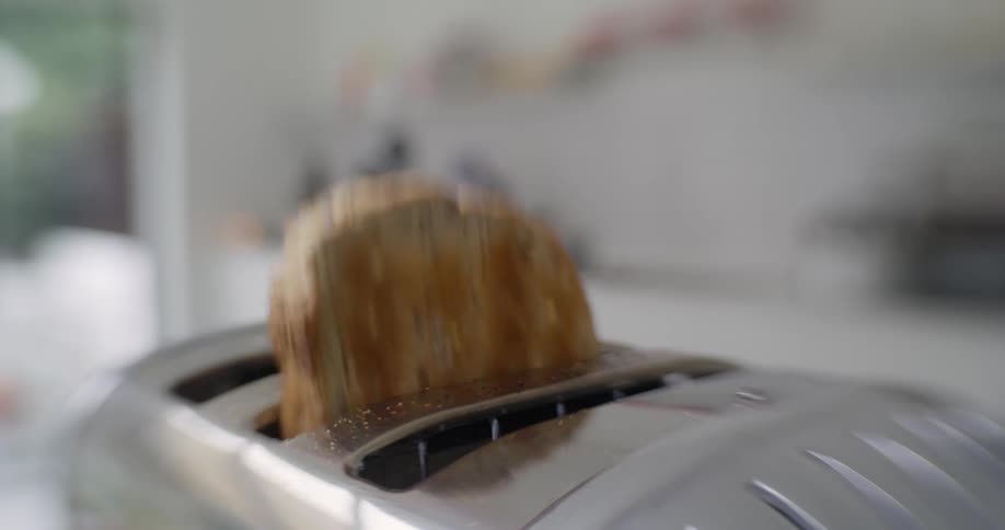 A piece of toast pops out of a stainless steel toaster