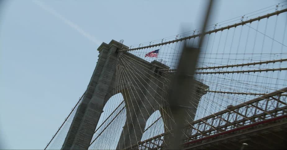 An american flag blows in the wind on the top of a bridge