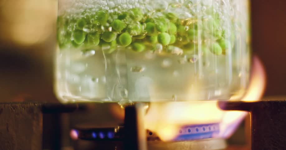 Peas boiling in a glass container on a gas burner