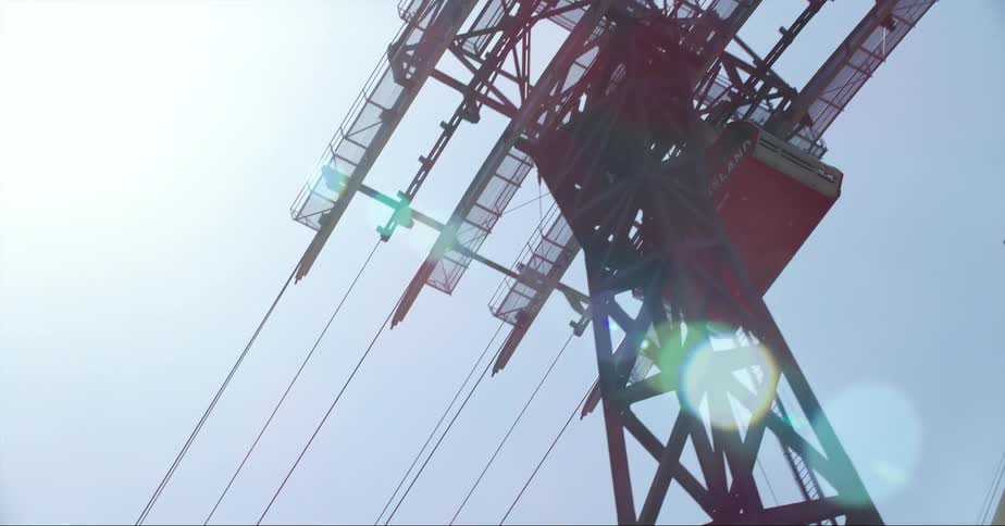 A cable car glides across a cable and past a tower as the sun shines in the sky