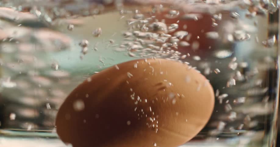 An egg being placed in a pot of boiling water